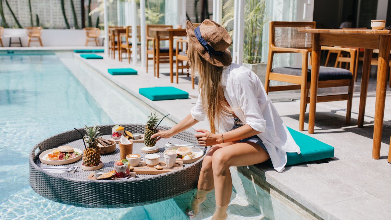 Female guest sitting at hotel pool area with breakfast board | Hotel Package Ideas