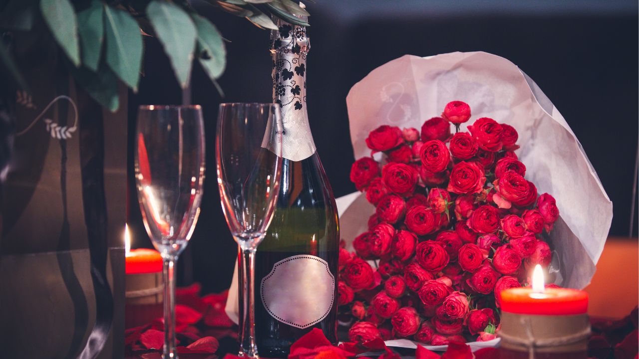 Two champagne glasses with a bottle of champagne, red roses, and two red lit candles | Hotel Package Ideas